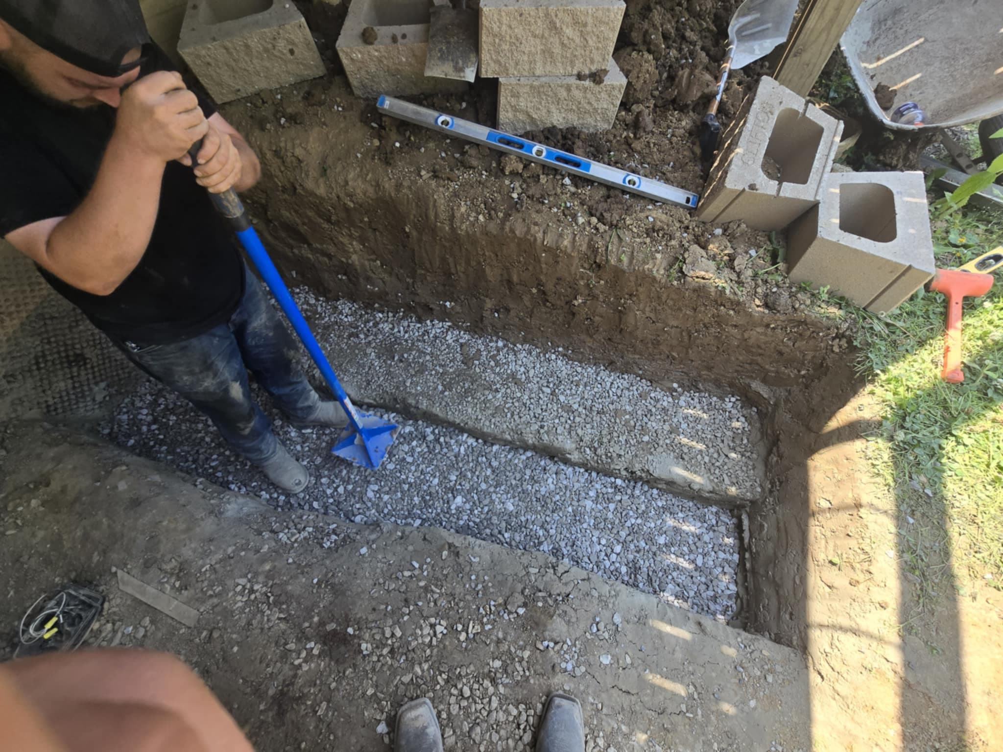 Worker compacting gravel base for retaining wall installation