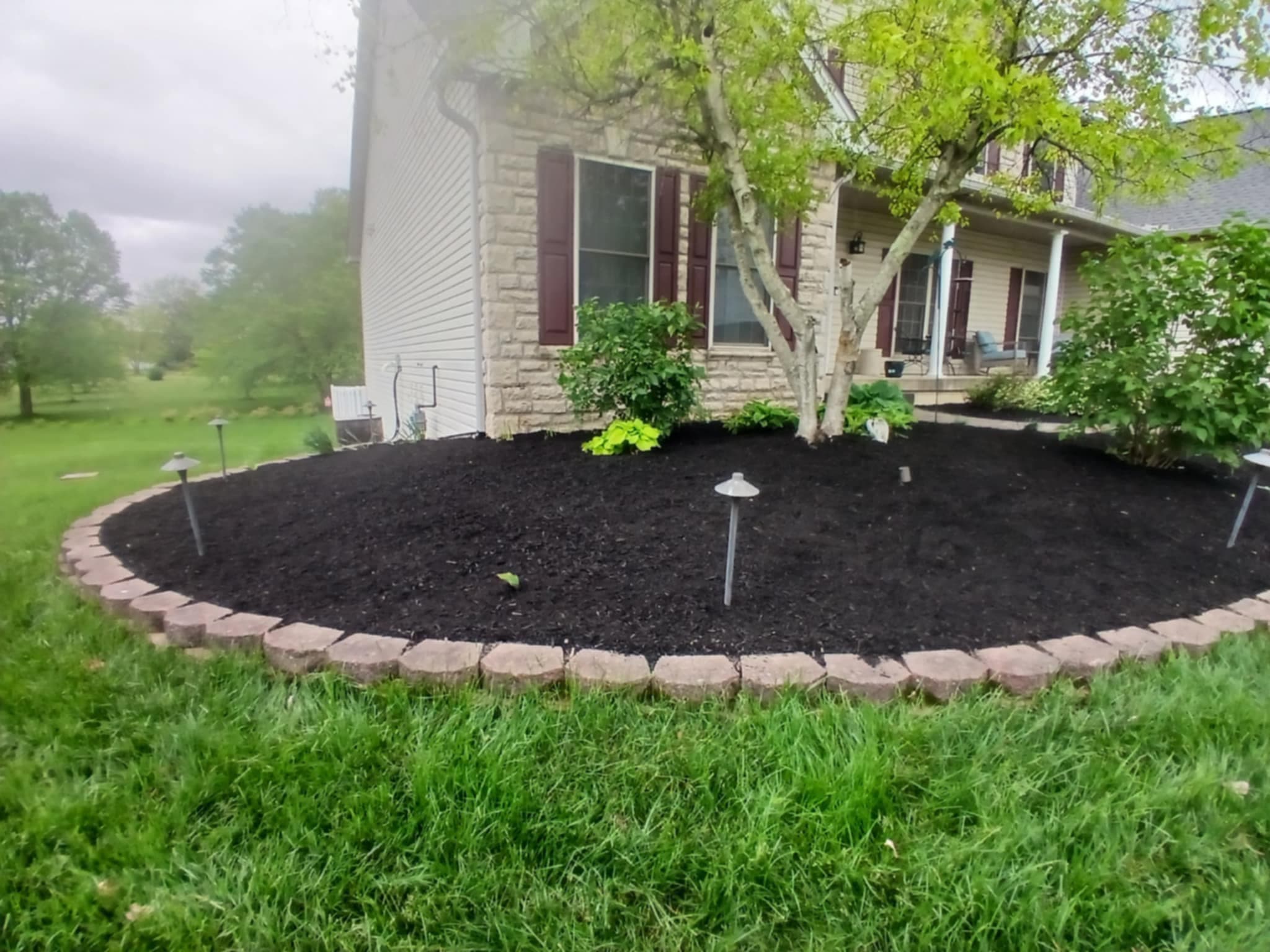 Large curved mulch bed with stone border and foundation shrubs